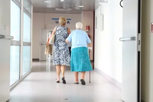 Senior Woman WithDaughter Walking Down Hospital Corridor Senior Woman WithDaughter Walking Down Hospital Corridor