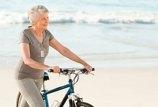 A happy woman with her PAX mobile medical alert on the beach with her bike A happy woman with her PAX mobile medical alert on the beach with her bike