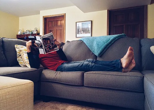 Man lounging on couch reading magazine Man lounging on couch reading magazine